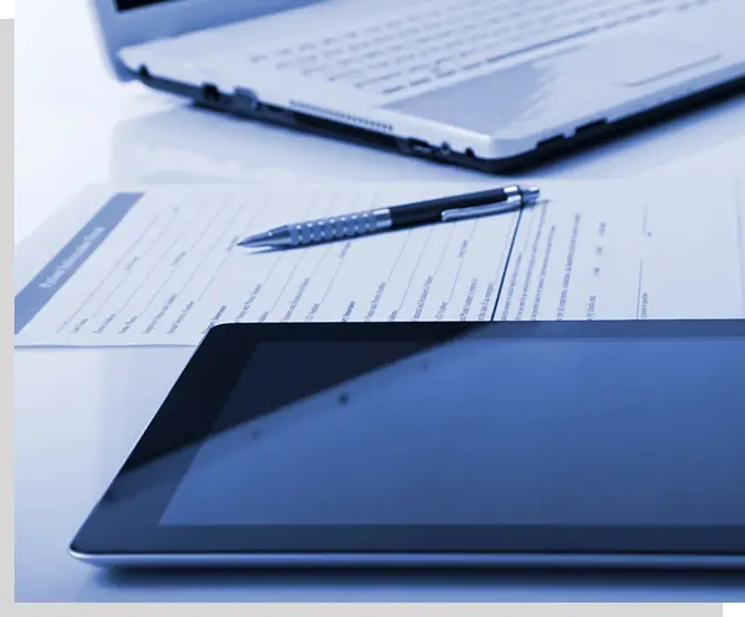 A tablet and laptop on top of papers.